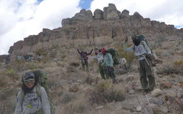 a group of gap year students descend from a rock formation in the desert on an outward bound semester expedition